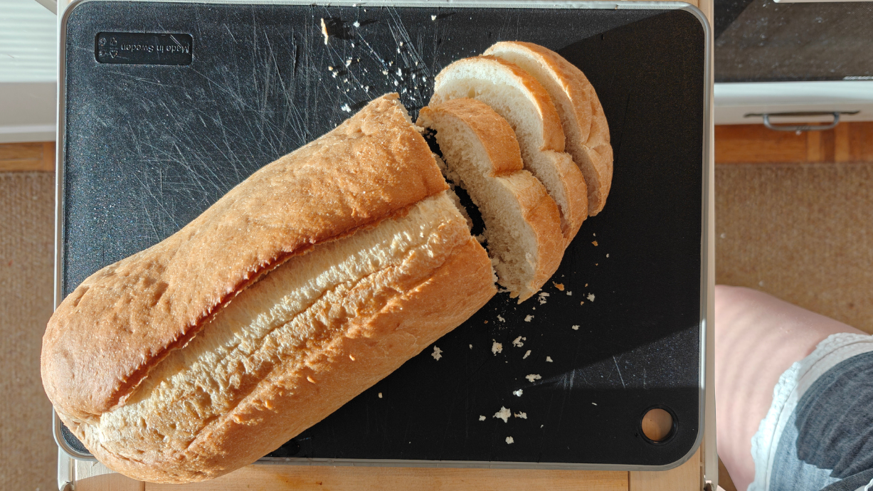 Pitkä vaalea leipä osittain viipaloituna mustalla leikkuualustalla
