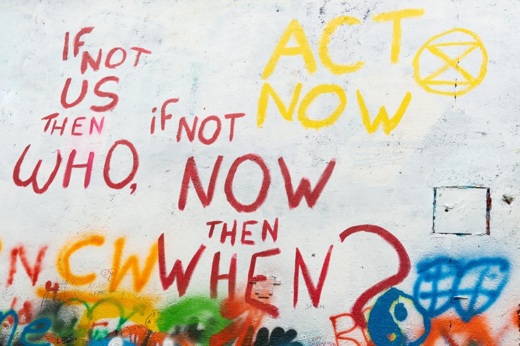 Graffiti: If not us, then who, if not now then when? Act now ja Elokapinan logo.
