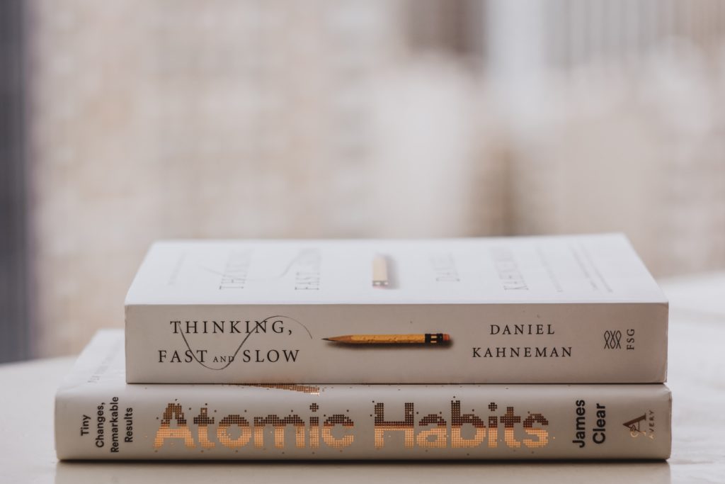 Kuva Atomic Habits -kirjasta ja Kahnemanin Thinking Fast and slow teoksesta.