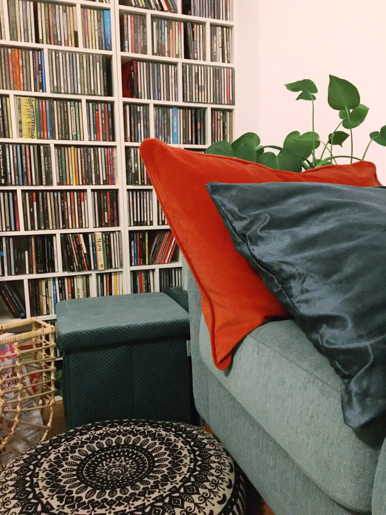Kuva olohuoneestamme sohvasta, tyynyistä ja huonekasvista sekä erilaisista säilytysratkaisuista.