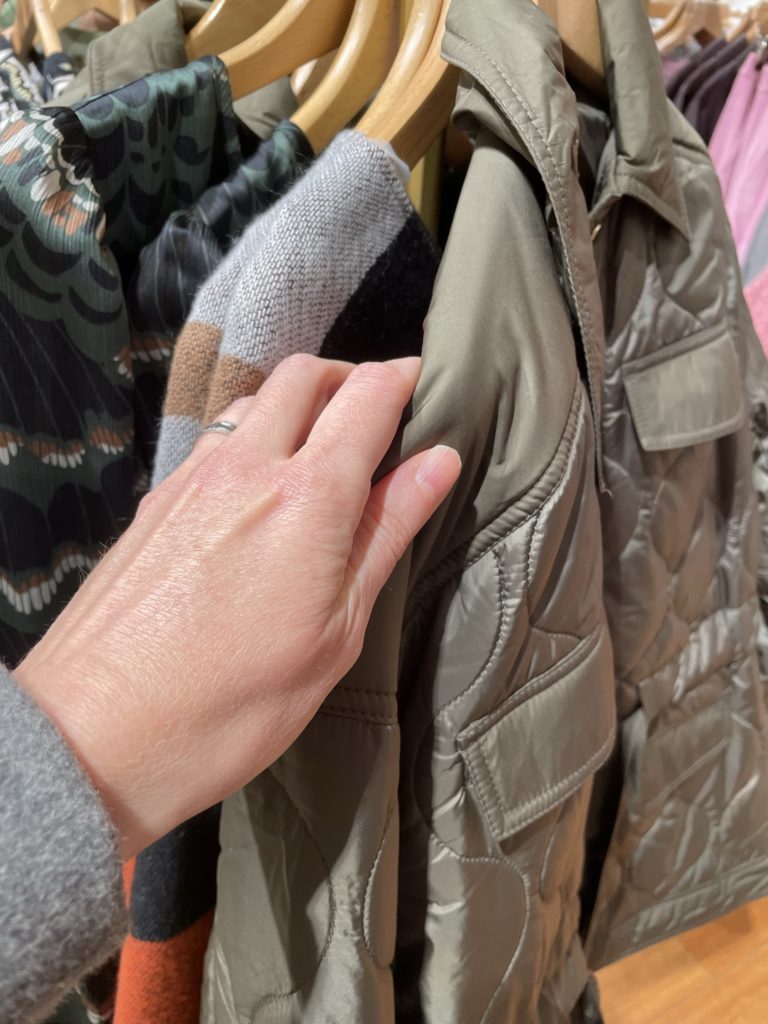 Kuva vaatekaupan rekistä ja kädestä, joka käy rekillä olevia vaatteita läpi.
